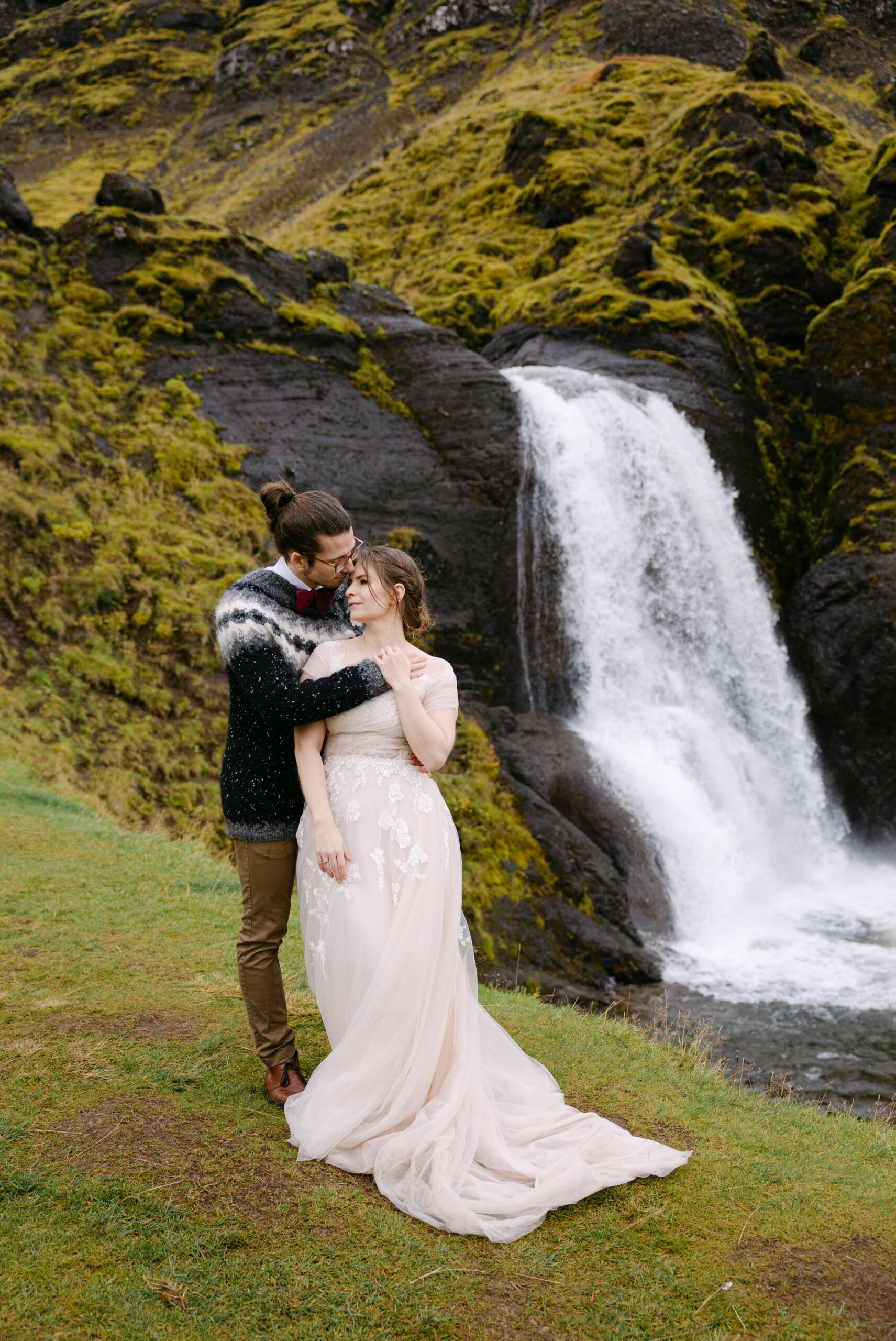 A couple stands in front of a waterfall in Iceland in their wedding attire